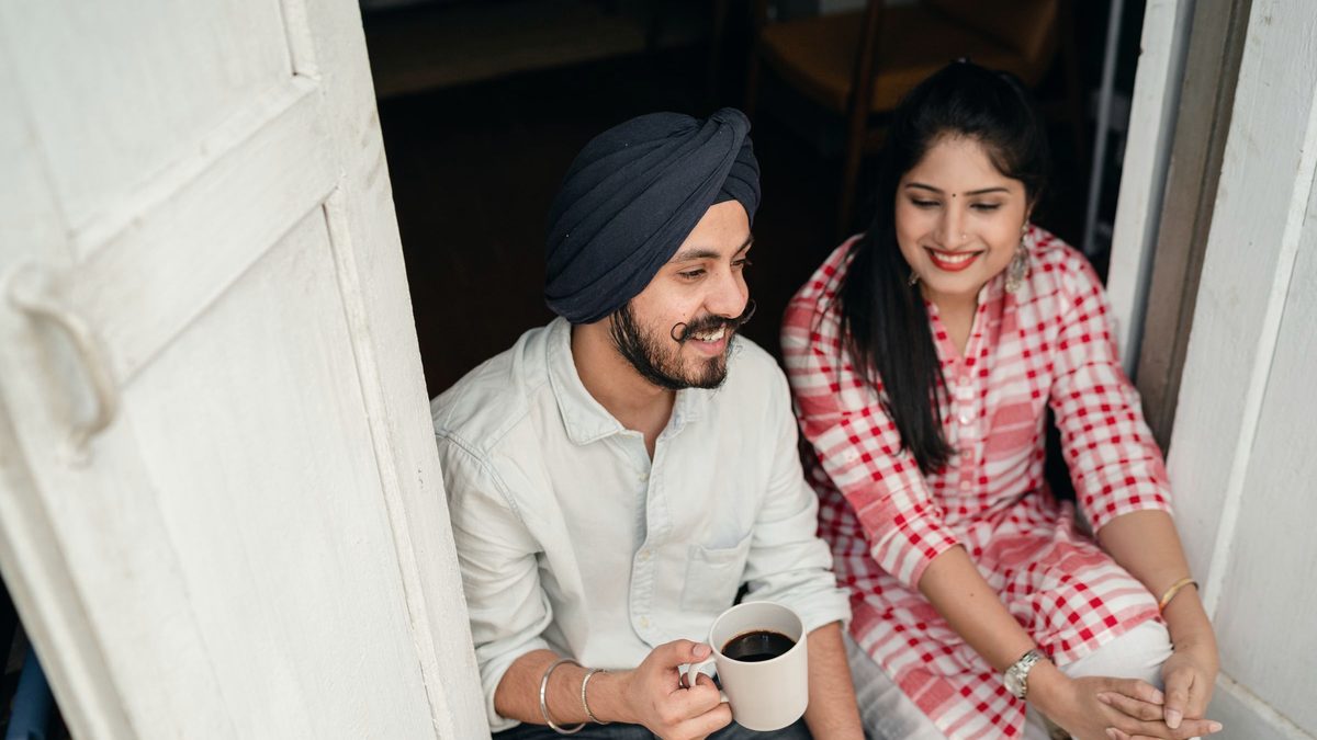 Un couple assis sur le pas de la porte, une tasse de café à la main, qui discute en souriant